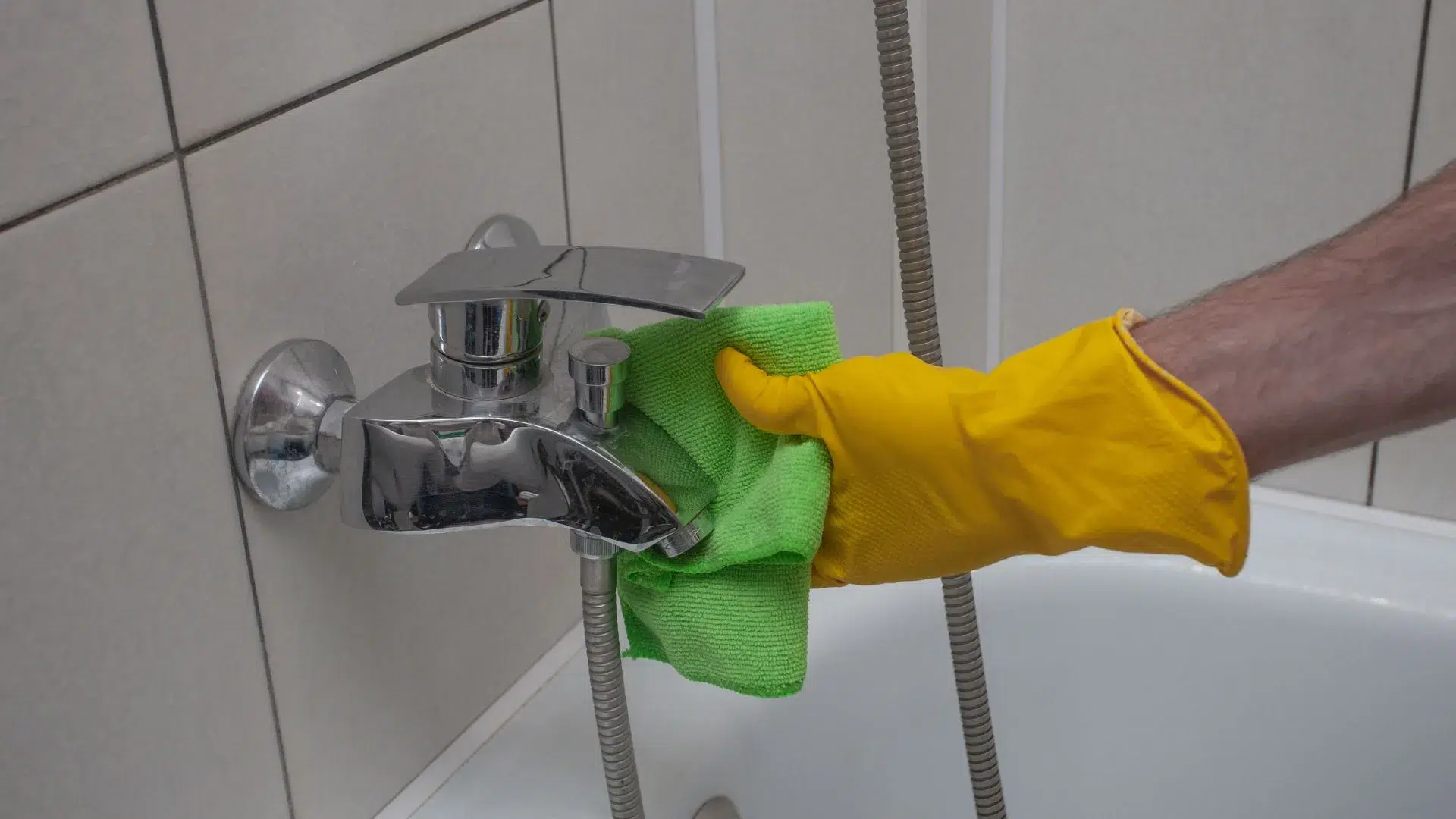 Persona limpiando una llave de baño con guantes y trapo verde, ilustrando cómo quitar el sarro del baño de grifos y superficies cromadas.