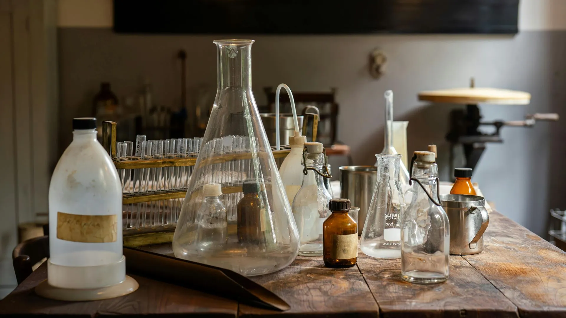 Utensilios y frascos de laboratorio sobre una mesa de madera, representando la práctica de la química antigua.