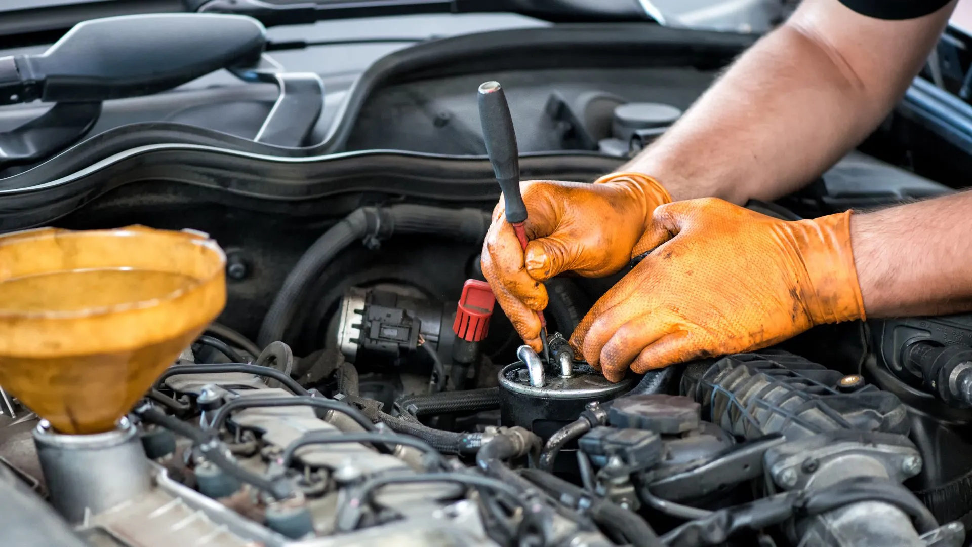 Mecánico trabajando en motor con guantes manchados de grasa automotriz, ejemplo del uso y limpieza de este lubricante en talleres de mantenimiento.